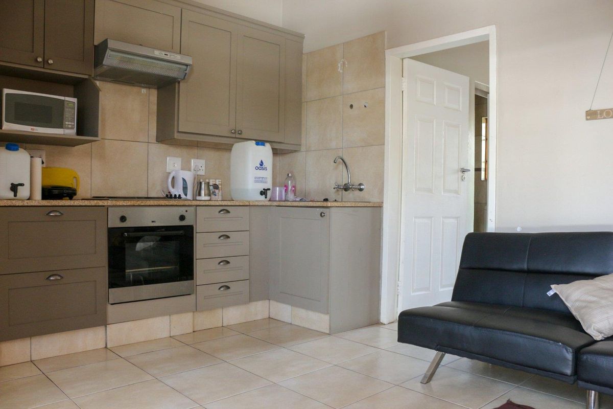 Compact open-plan kitchen featuring neutral cabinetry, built-in oven, extractor fan, and tiled flooring, seamlessly connecting to the living area.