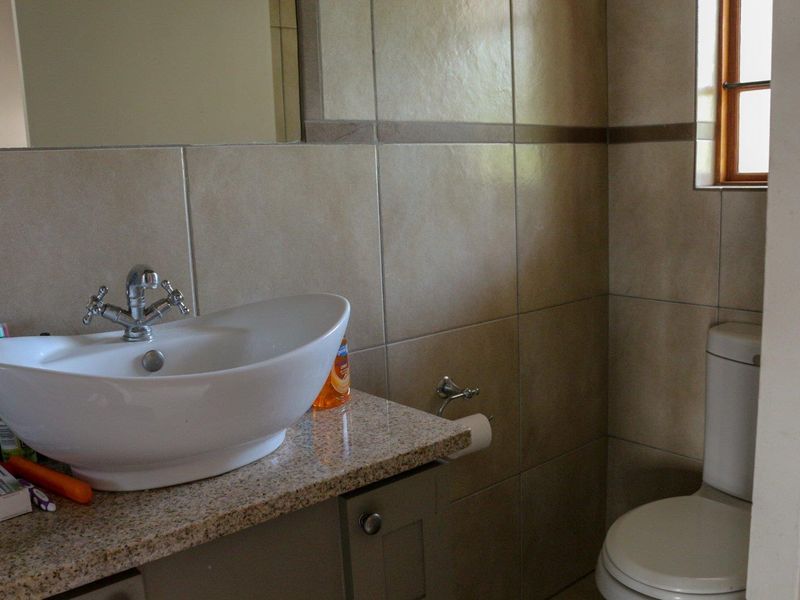 A functional bathroom featuring a vessel sink on a granite vanity top, wall-mounted mirror, and a standard toilet with neutral wall tiling.