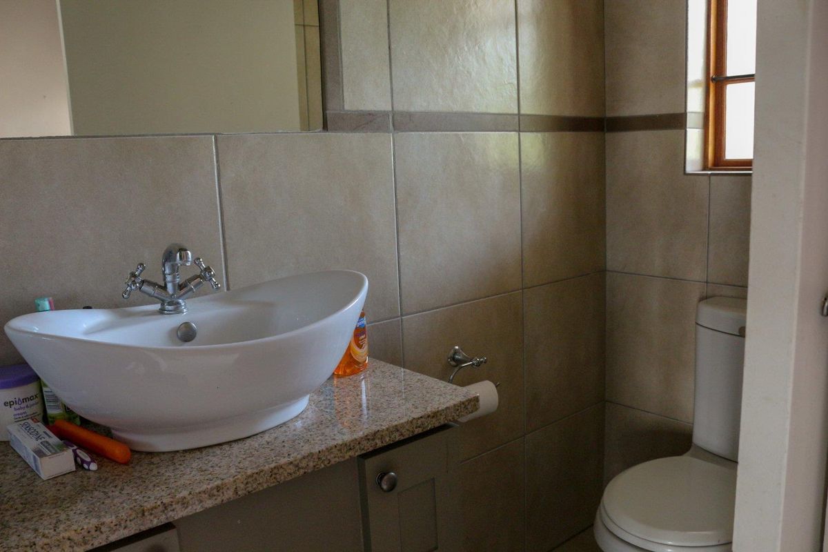 A functional bathroom featuring a vessel sink on a granite vanity top, wall-mounted mirror, and a standard toilet with neutral wall tiling.
