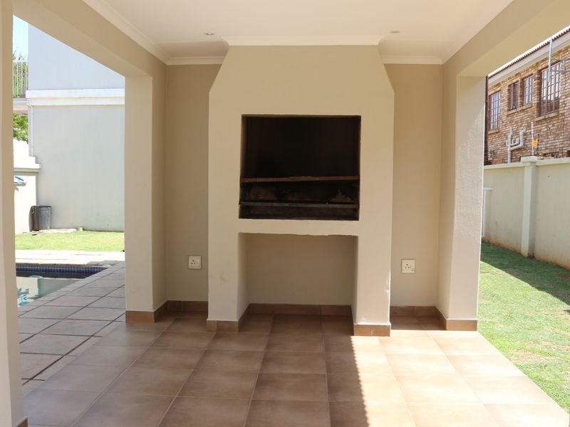 Covered patio area featuring a built-in braai, tiled flooring, and direct access to the garden and swimming pool.