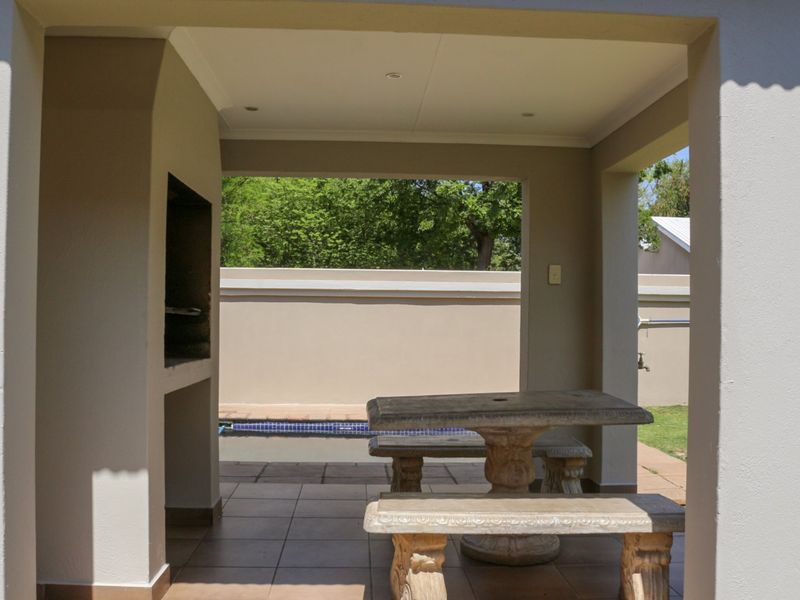 Covered patio area featuring a built-in braai, tiled flooring, and direct access to the outdoor pool and garden space.
