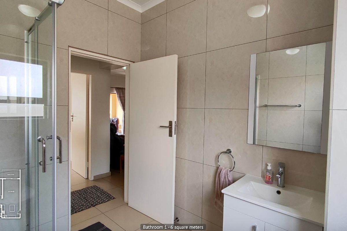 A clean, modern bathroom featuring a glass shower enclosure, a vanity cabinet with a basin, and neutral wall tiling.
