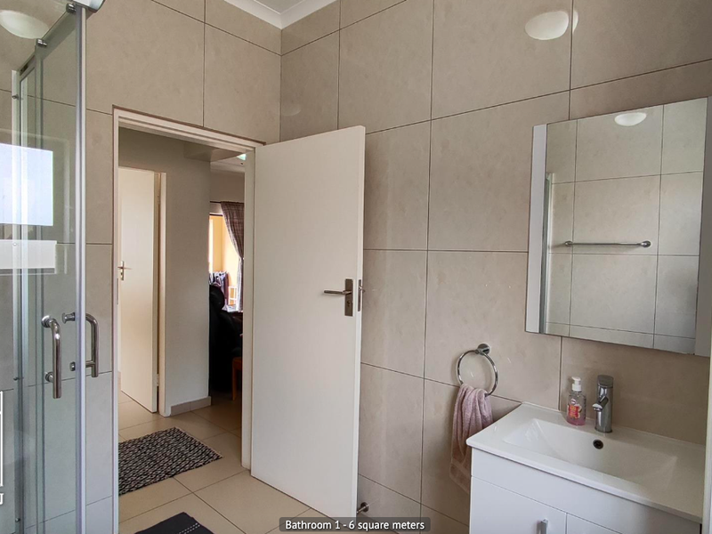 A clean, modern bathroom featuring a glass shower enclosure, a vanity cabinet with a basin, and neutral wall tiling.
