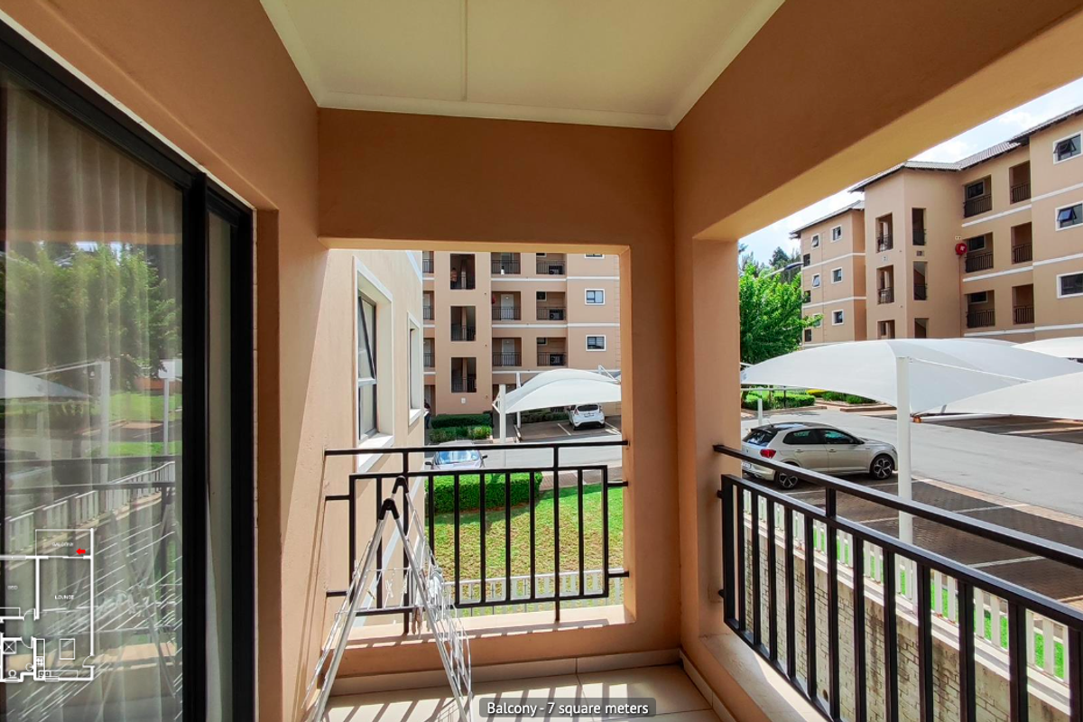 A covered balcony featuring tiled flooring and a metal balustrade, offering views of the complex parking area and surrounding townhouse units.