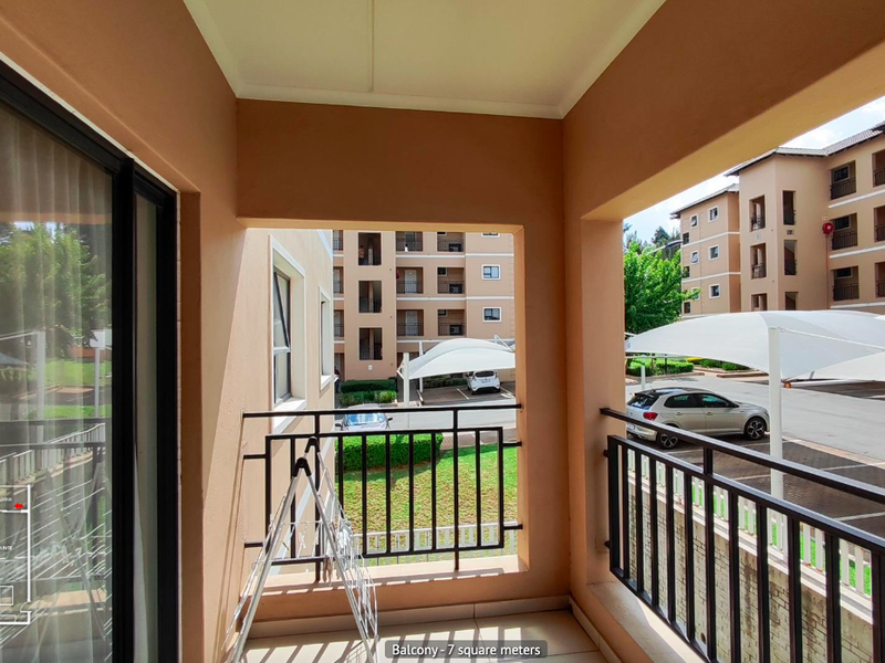 A covered balcony featuring tiled flooring and a metal balustrade, offering views of the complex parking area and surrounding townhouse units.