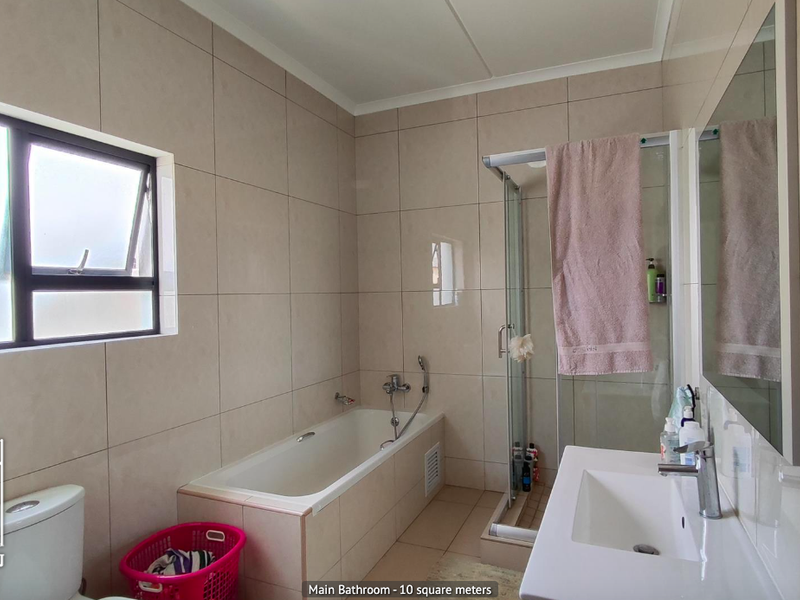 A well-maintained main bathroom featuring a built-in bathtub, separate glass shower enclosure, and a modern wall-mounted vanity basin with neutral wall tiling.