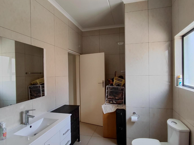 Modern bathroom featuring floor-to-ceiling wall tiles, a sleek vanity with basin, wall-mounted mirror, and a standard toilet.
