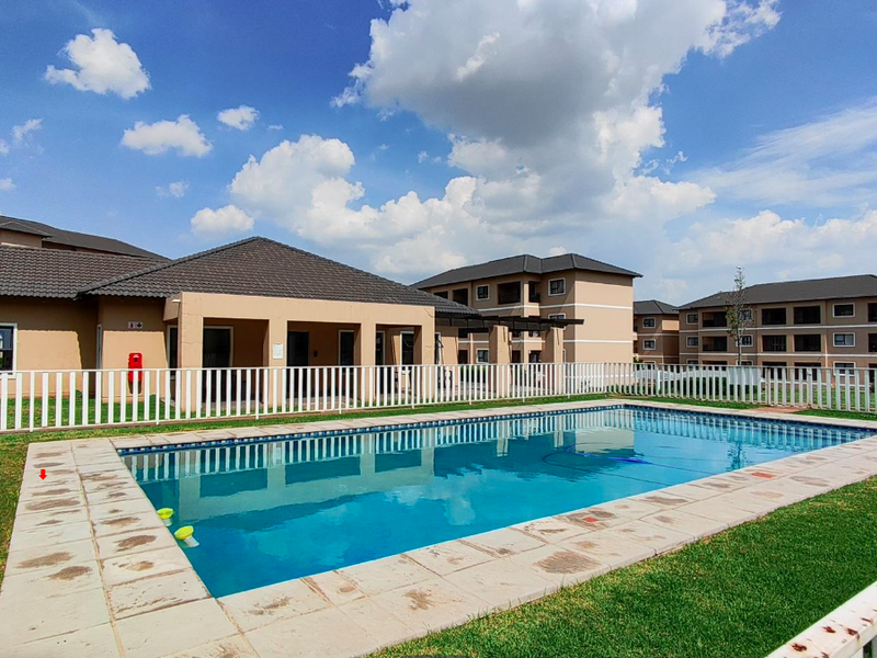 Communal swimming pool area featuring a paved surround, white perimeter fencing, and views of the surrounding townhouse complex buildings.