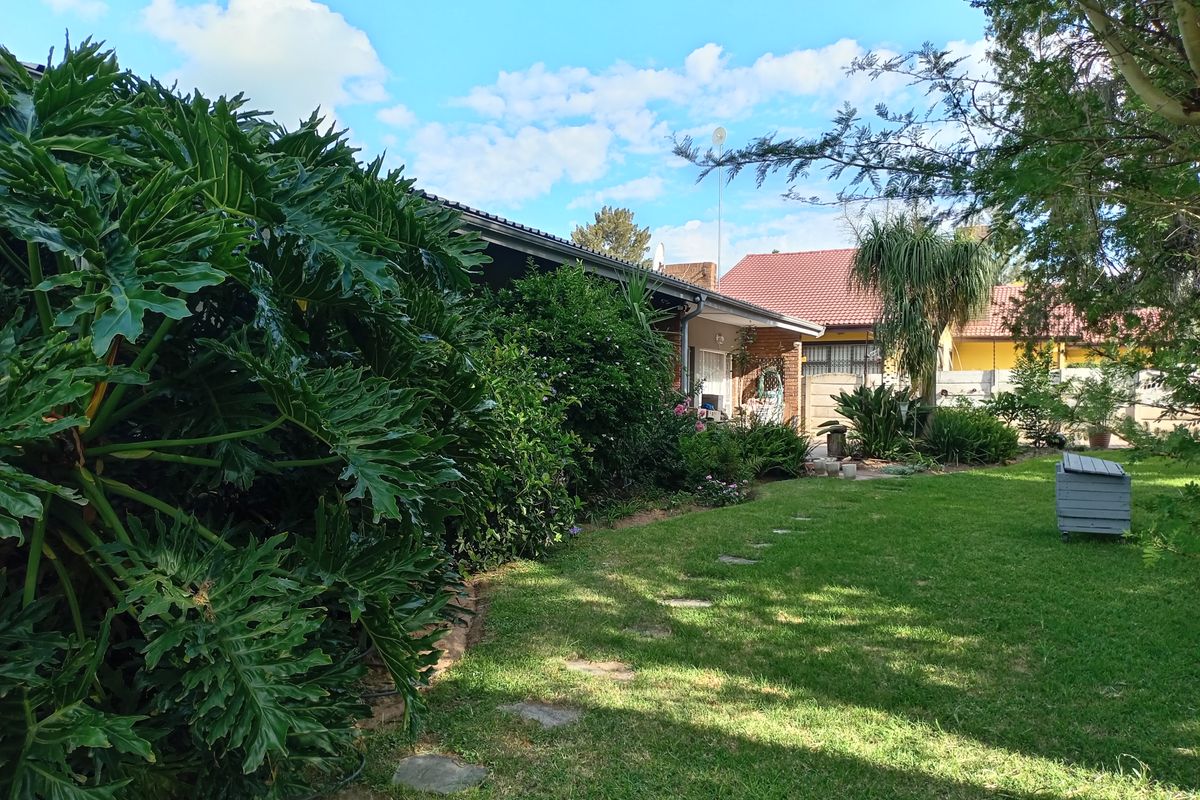 A view of the rear garden featuring a well-maintained lawn, stone pathway, and the rear brick facade of the house with a tiled roof.