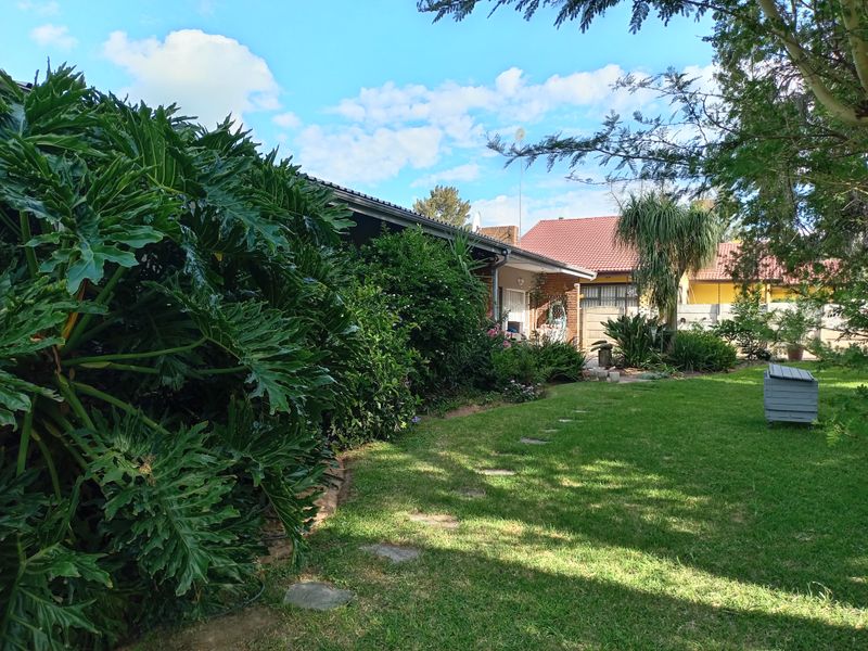 A view of the rear garden featuring a well-maintained lawn, stone pathway, and the rear brick facade of the house with a tiled roof.