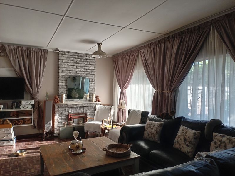 A cozy living room featuring a brick fireplace, parquet flooring, and large windows with curtains.