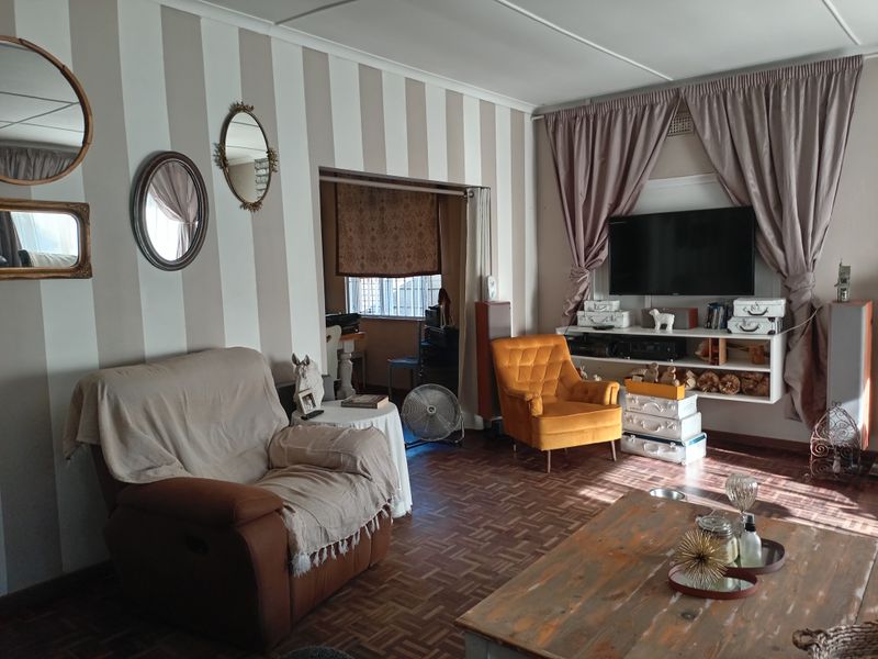 A living room featuring classic parquet flooring and built-in wall shelving, with a connected adjacent space visible through the doorway.