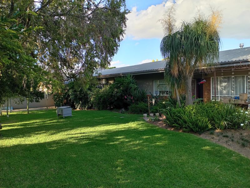 Front view of a single-story house featuring a metal roof, brick exterior, and a well-maintained lawn with established garden beds.