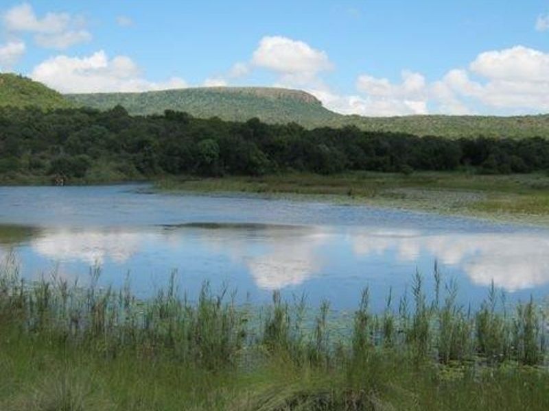 A scenic view of a natural dam surrounded by indigenous vegetation and rolling hills, showcasing the tranquil landscape of the vacant residential land.