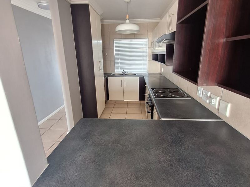 A functional kitchen featuring dark laminate countertops, built-in cabinetry, an electric hob with extractor fan, and a stainless steel sink.