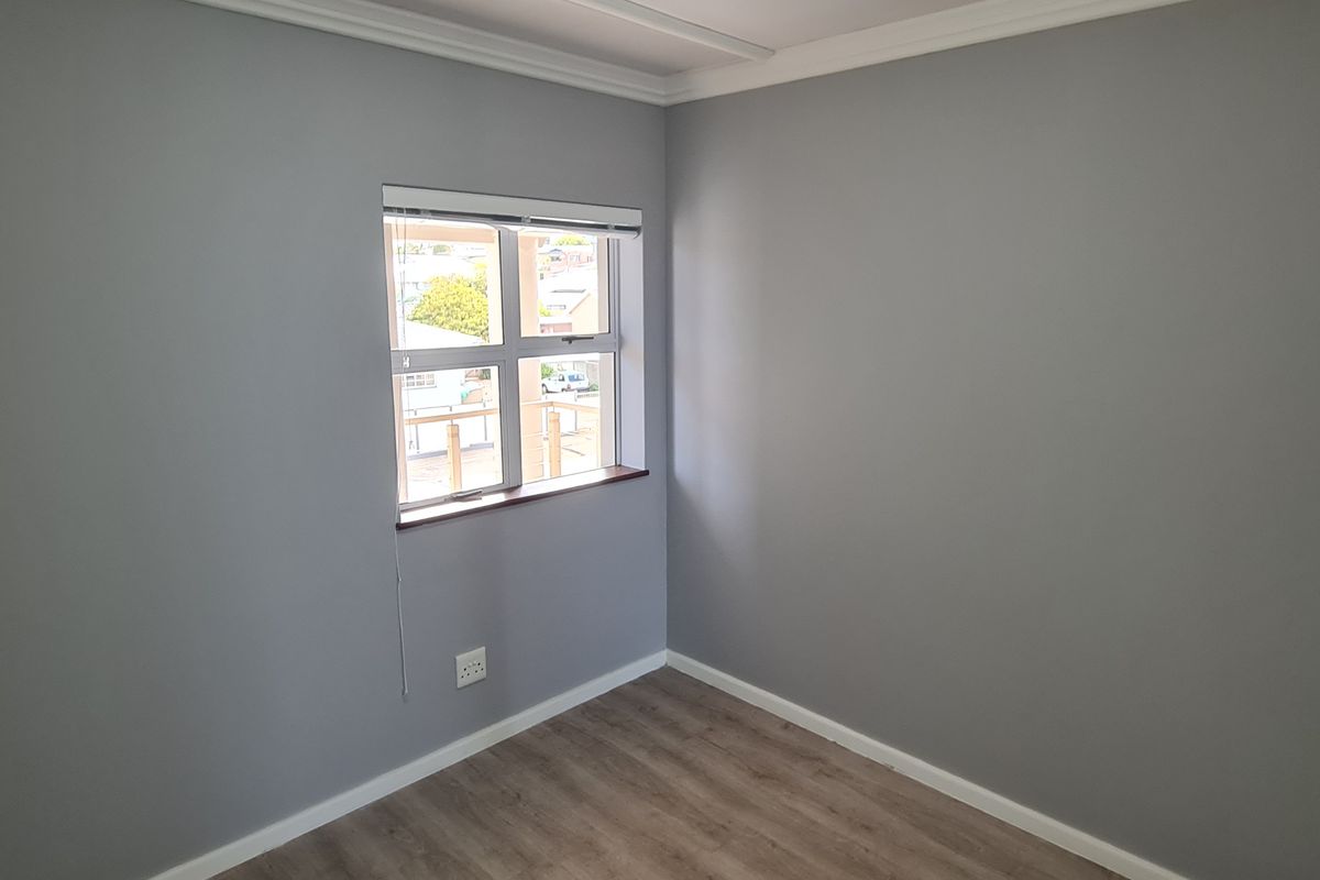 A clean, empty bedroom featuring neutral grey walls, laminate wood-look flooring, and a window with a fitted blind.
