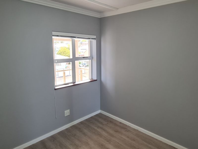 A clean, empty bedroom featuring neutral grey walls, laminate wood-look flooring, and a window with a fitted blind.
