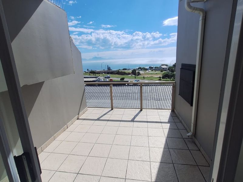 A clean, tiled balcony featuring a protective railing and expansive coastal views, providing a pleasant outdoor space for relaxation.
