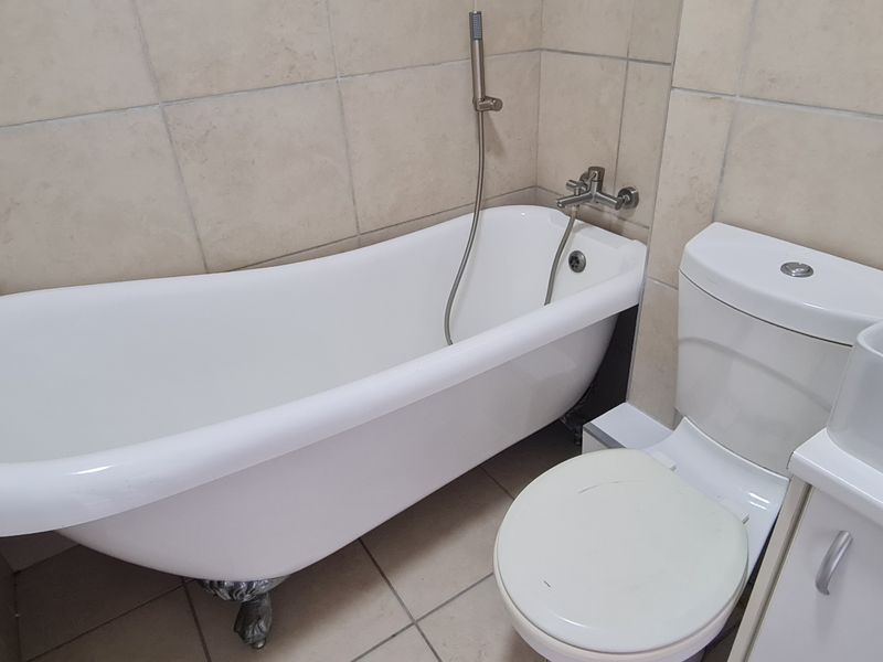 A bathroom featuring a classic clawfoot bathtub, a modern vanity basin, and a standard toilet with neutral wall and floor tiling.