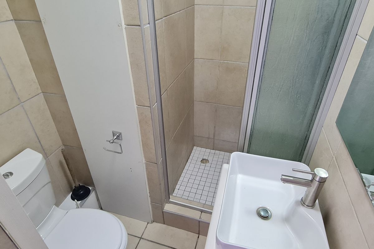 Compact bathroom featuring a shower enclosure, toilet, and basin with modern mixer tap, finished with neutral wall and floor tiling.