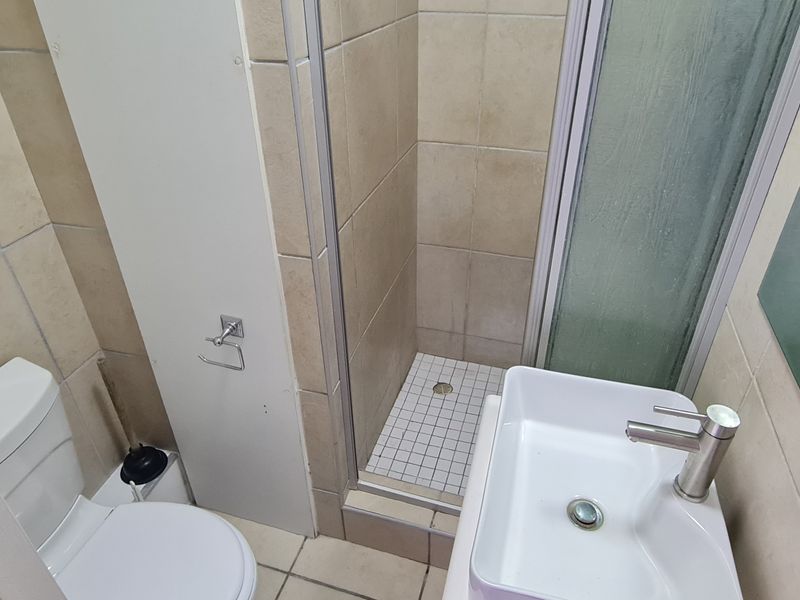 Compact bathroom featuring a shower enclosure, toilet, and basin with modern mixer tap, finished with neutral wall and floor tiling.