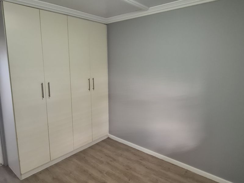 A clean, empty bedroom featuring light-toned built-in cupboards, modern laminate flooring, and neutral grey walls, offering a versatile space ready for personalization.