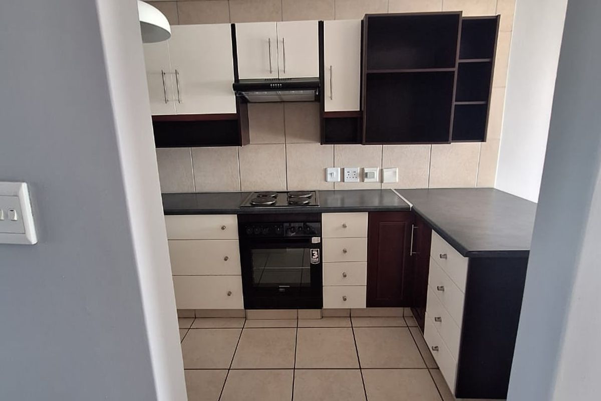 A clean, functional kitchen featuring two-tone cabinetry, built-in oven and hob, tiled backsplash, and neutral floor tiles.