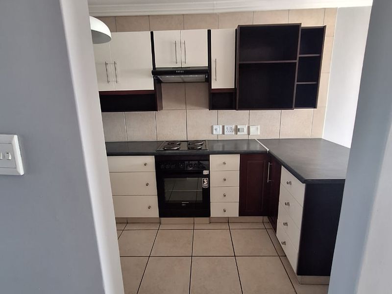 A clean, functional kitchen featuring two-tone cabinetry, built-in oven and hob, tiled backsplash, and neutral floor tiles.
