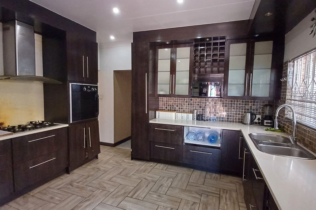 Modern kitchen featuring dark wood cabinetry, stone countertops, mosaic tile backsplash, built-in oven, gas hob, and herringbone floor tiles.