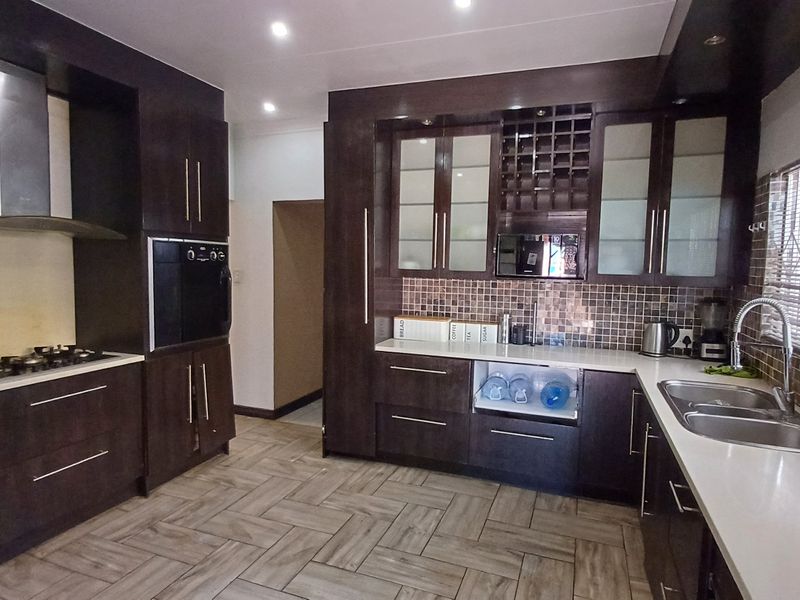 Modern kitchen featuring dark wood cabinetry, stone countertops, mosaic tile backsplash, built-in oven, gas hob, and herringbone floor tiles.