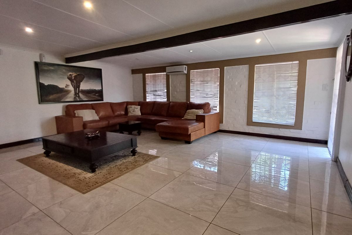 Spacious living room featuring large format floor tiles, a painted brick feature wall, exposed ceiling beam, and a wall-mounted air conditioning unit.