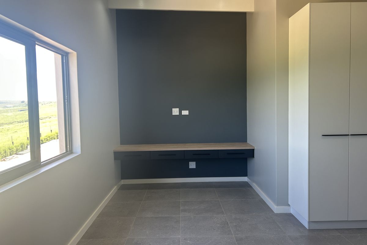 A modern, empty bedroom featuring a built-in desk, integrated wardrobe, tiled flooring, and a large window with natural light.
