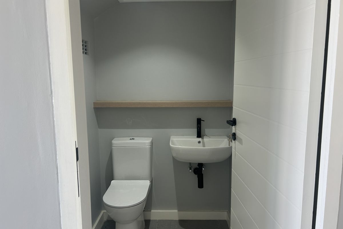 A modern, compact guest bathroom featuring a wall-mounted basin with black fixtures, a white toilet, and a floating timber shelf.