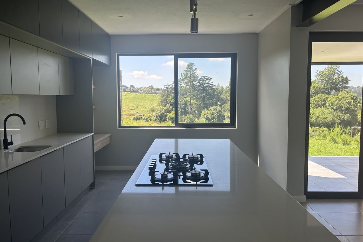 Modern kitchen featuring a central island with a gas hob, sleek cabinetry, quartz countertops, and large windows offering scenic views.