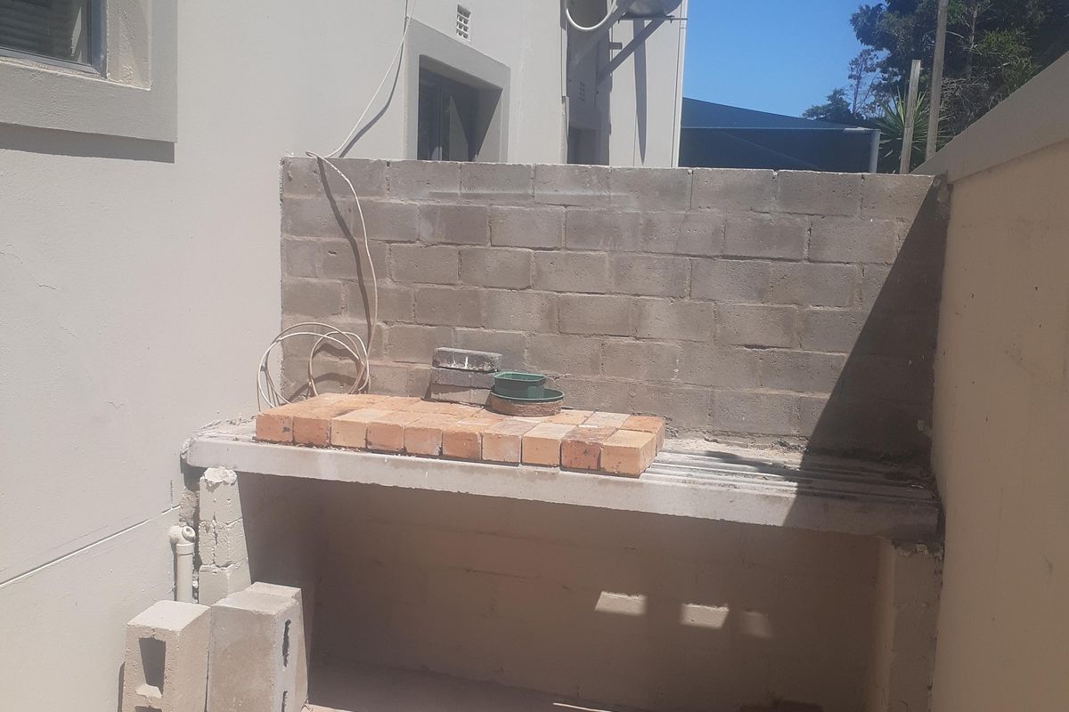 Rear exterior area featuring a basic built-in braai structure, paved flooring, and wall-mounted solar geyser unit.