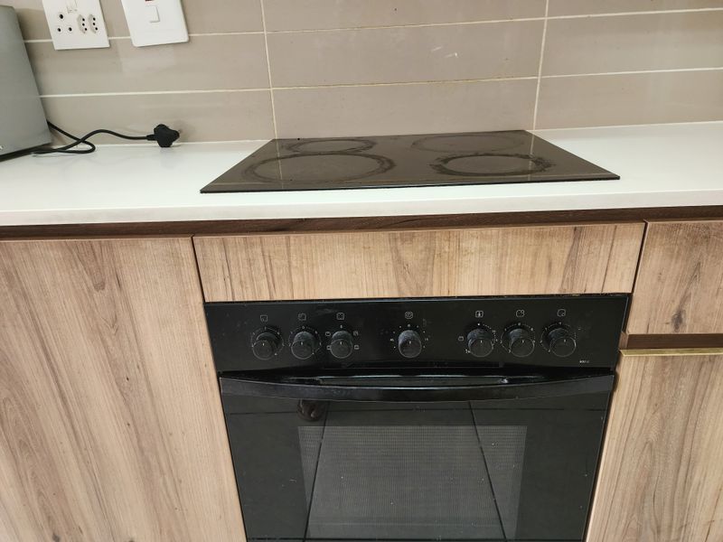 A functional kitchen area featuring a built-in oven, electric hob, stone countertop, and modern wood-look cabinetry with a tiled backsplash.