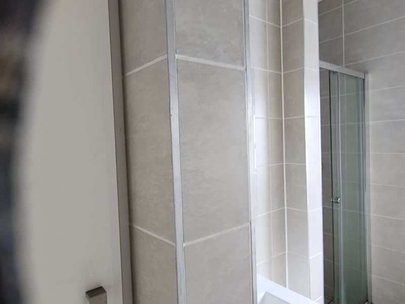 A clean bathroom featuring neutral wall tiling and a glass-enclosed shower unit.
