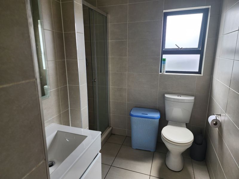 A modern bathroom featuring a shower enclosure, vanity basin, and toilet with neutral floor-to-ceiling tiling and a frosted window for natural light.