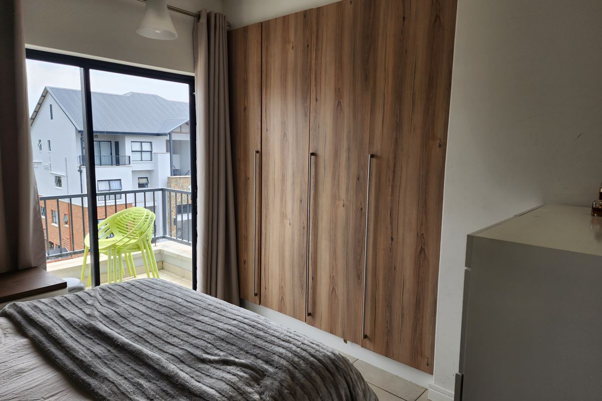 A well-maintained bedroom featuring modern wood-finish built-in cupboards and a sliding glass door providing access to a private balcony.