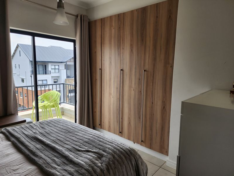 A well-maintained bedroom featuring modern wood-finish built-in cupboards and a sliding glass door providing access to a private balcony.