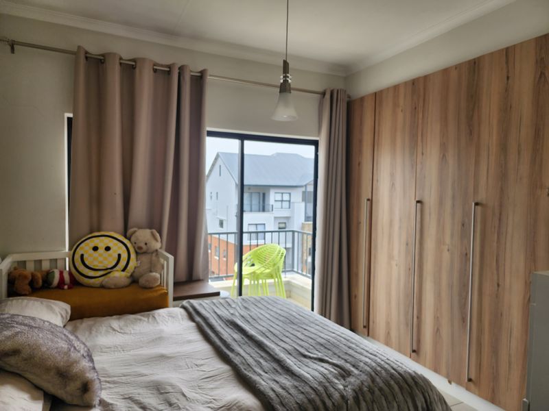A well-maintained bedroom featuring modern wood-finish built-in cupboards, a pendant light, and a sliding glass door providing access to a private balcony.