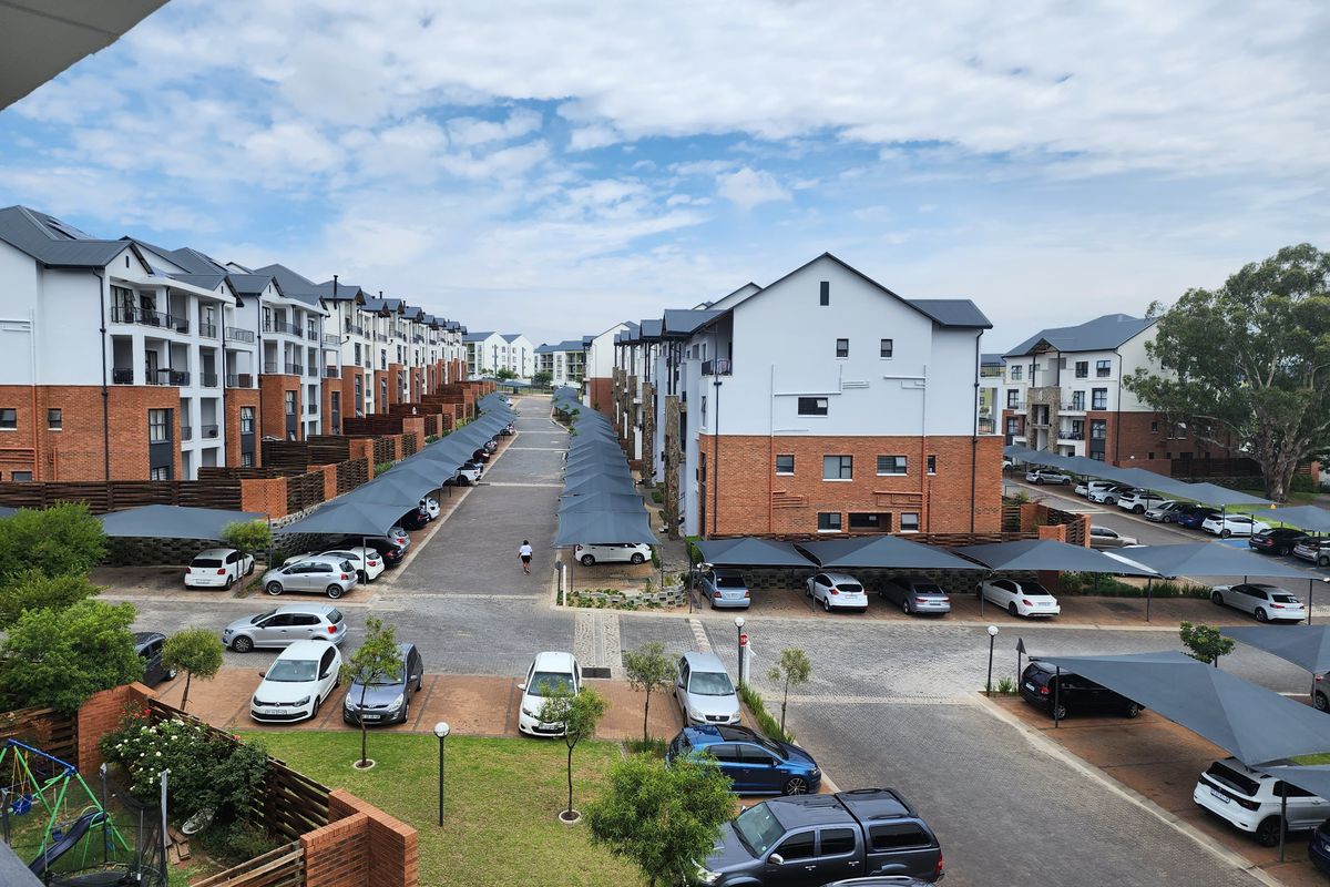 An elevated aerial view of a modern apartment complex featuring paved driveways, covered parking bays, and well-maintained communal garden areas.