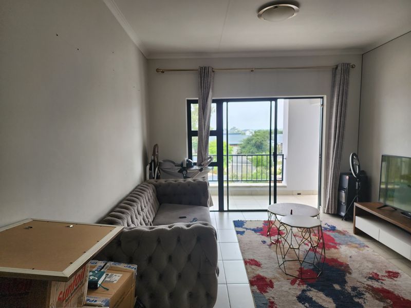 A living room featuring tiled flooring and a sliding glass door that opens onto a balcony, providing natural light and outdoor access.