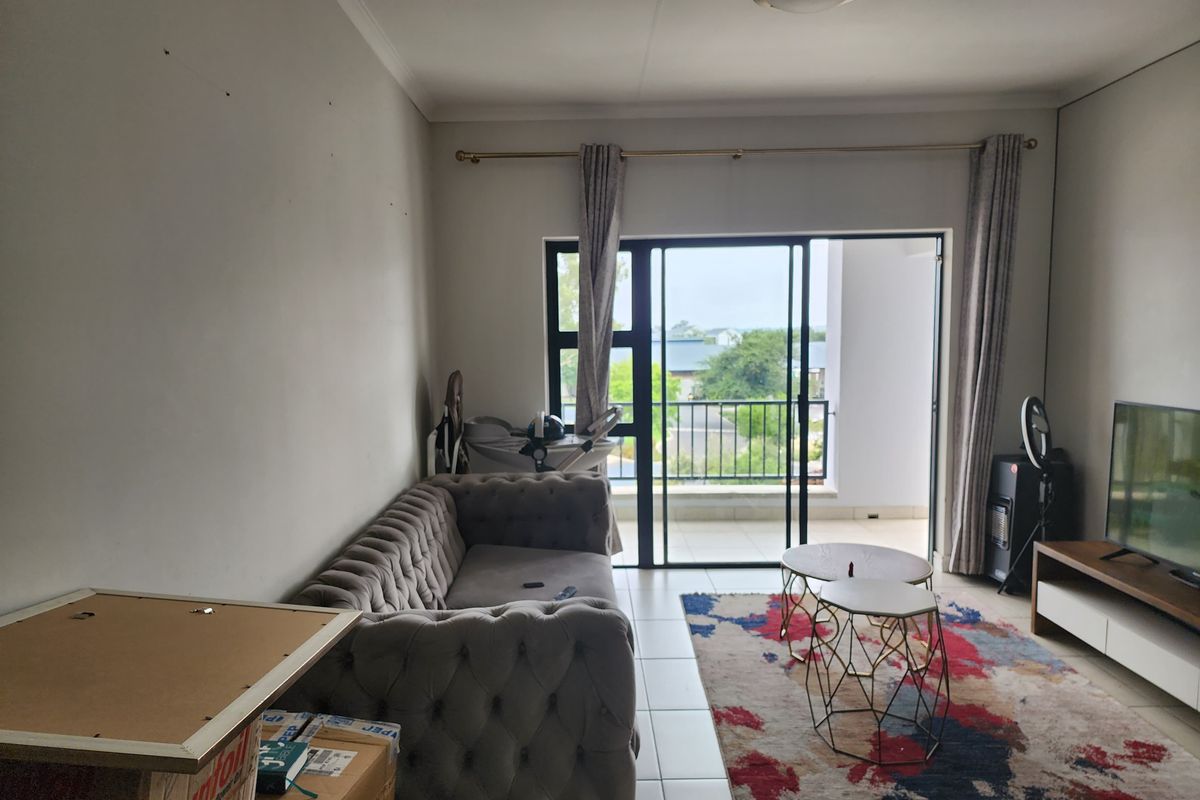 A living room featuring tiled flooring and a sliding glass door that opens onto a balcony, providing natural light and outdoor access.