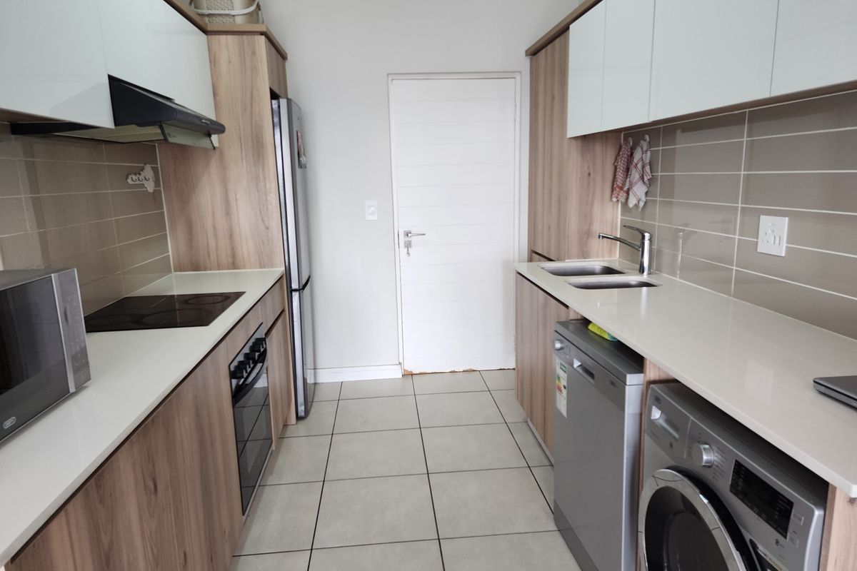 Modern galley-style kitchen featuring light wood-grain cabinetry, stone countertops, tiled backsplash, and integrated appliances with a clean, functional layout.