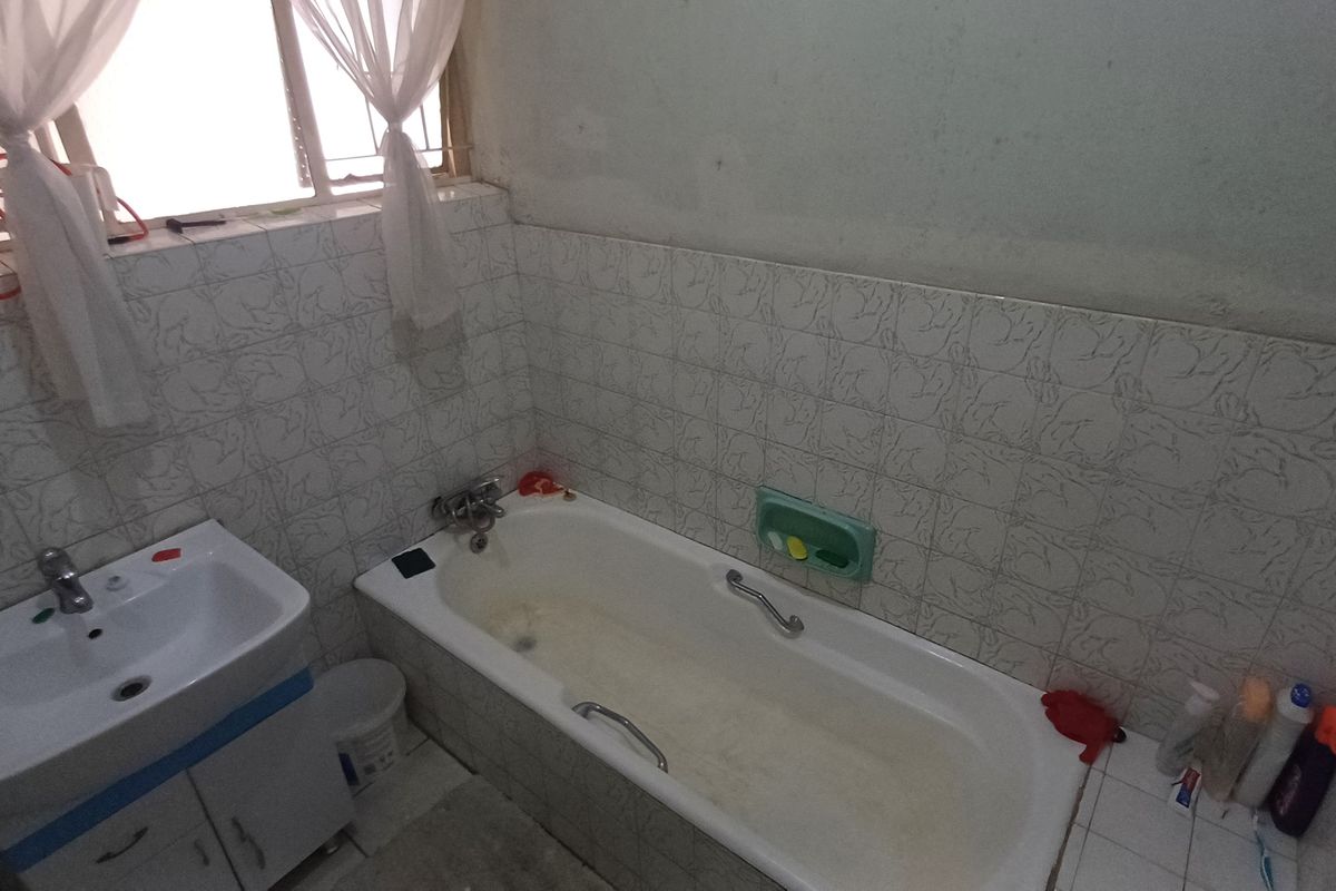 A functional bathroom featuring a standard bathtub, vanity basin, and tiled wall finishes, currently showing signs of age and wear.