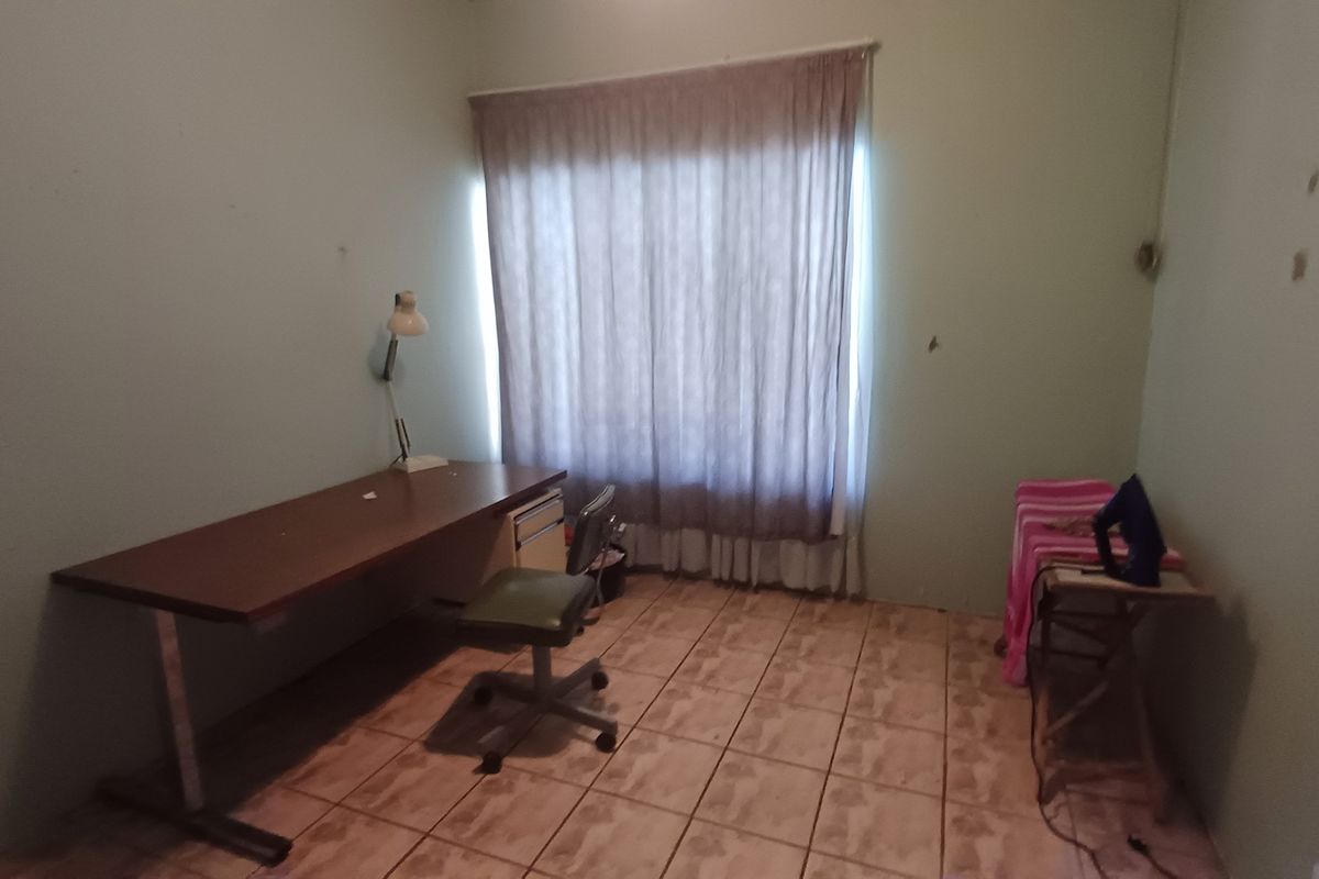 A bedroom featuring tiled flooring and a window with curtains, currently showing signs of wear on the wall surfaces.