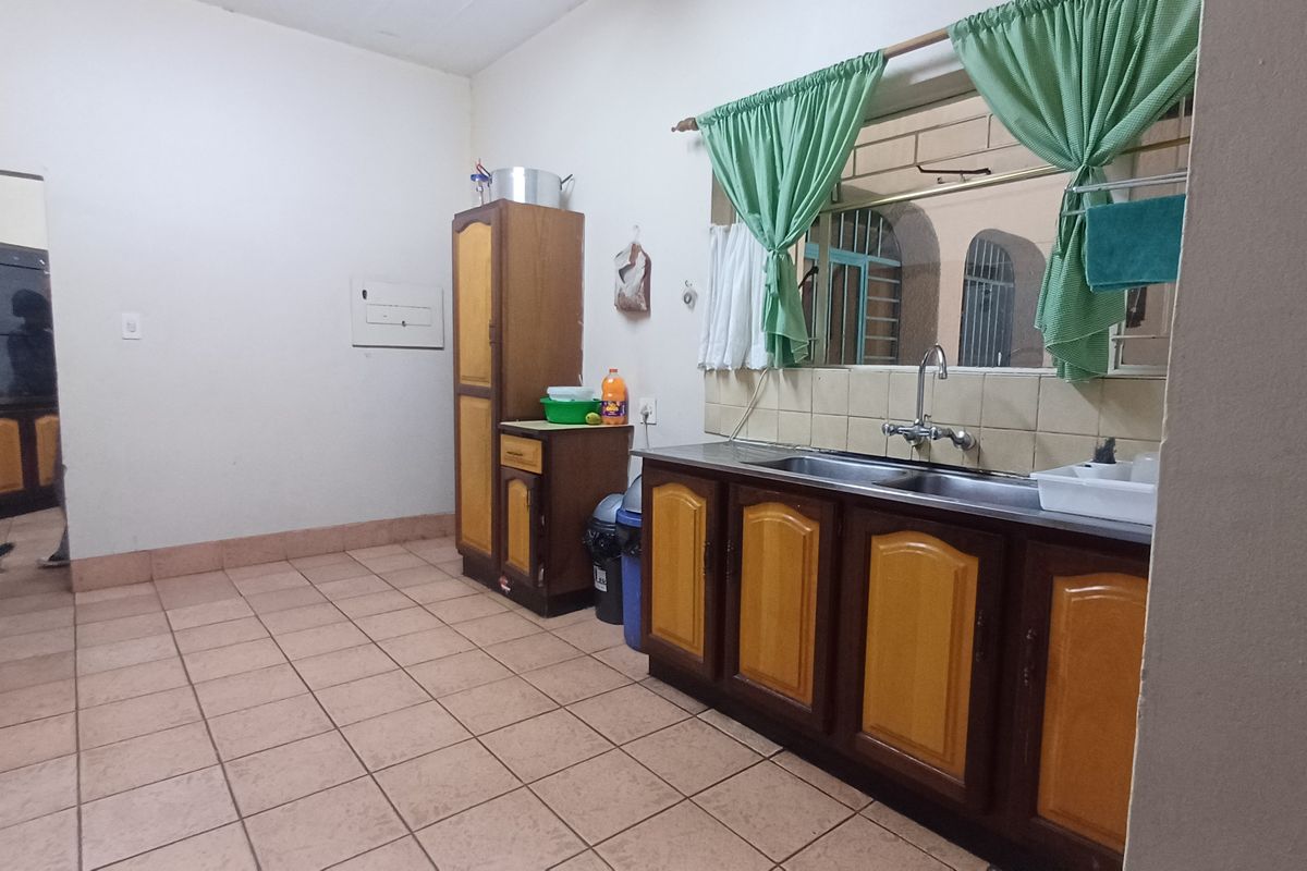 A functional kitchen featuring dated wooden cabinetry, a stainless steel sink, tiled flooring, and a tiled backsplash.