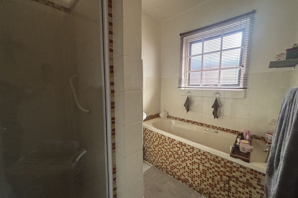 A functional bathroom featuring a built-in bathtub with mosaic tile detailing, a separate shower enclosure, and a window with fitted blinds.