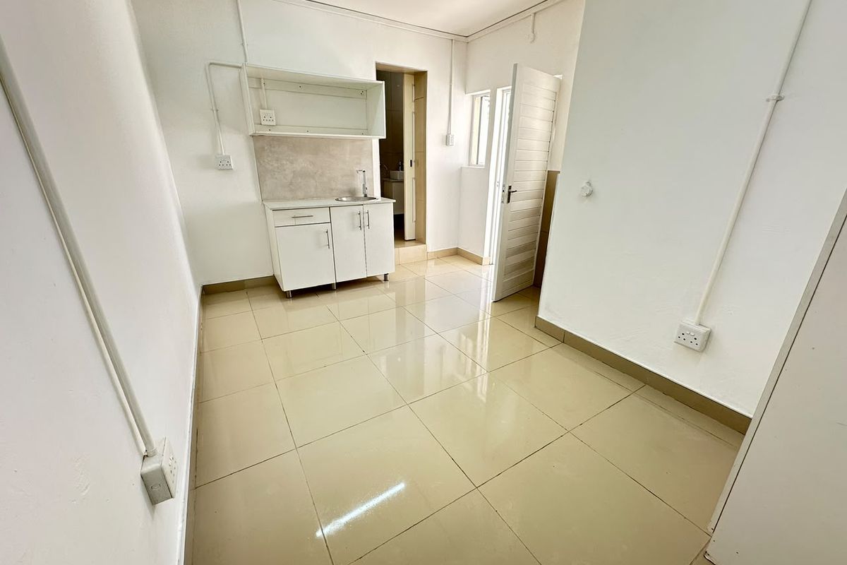 A compact, empty kitchenette area featuring tiled flooring, basic cabinetry with a sink, and exposed electrical conduit, providing a functional utility space.